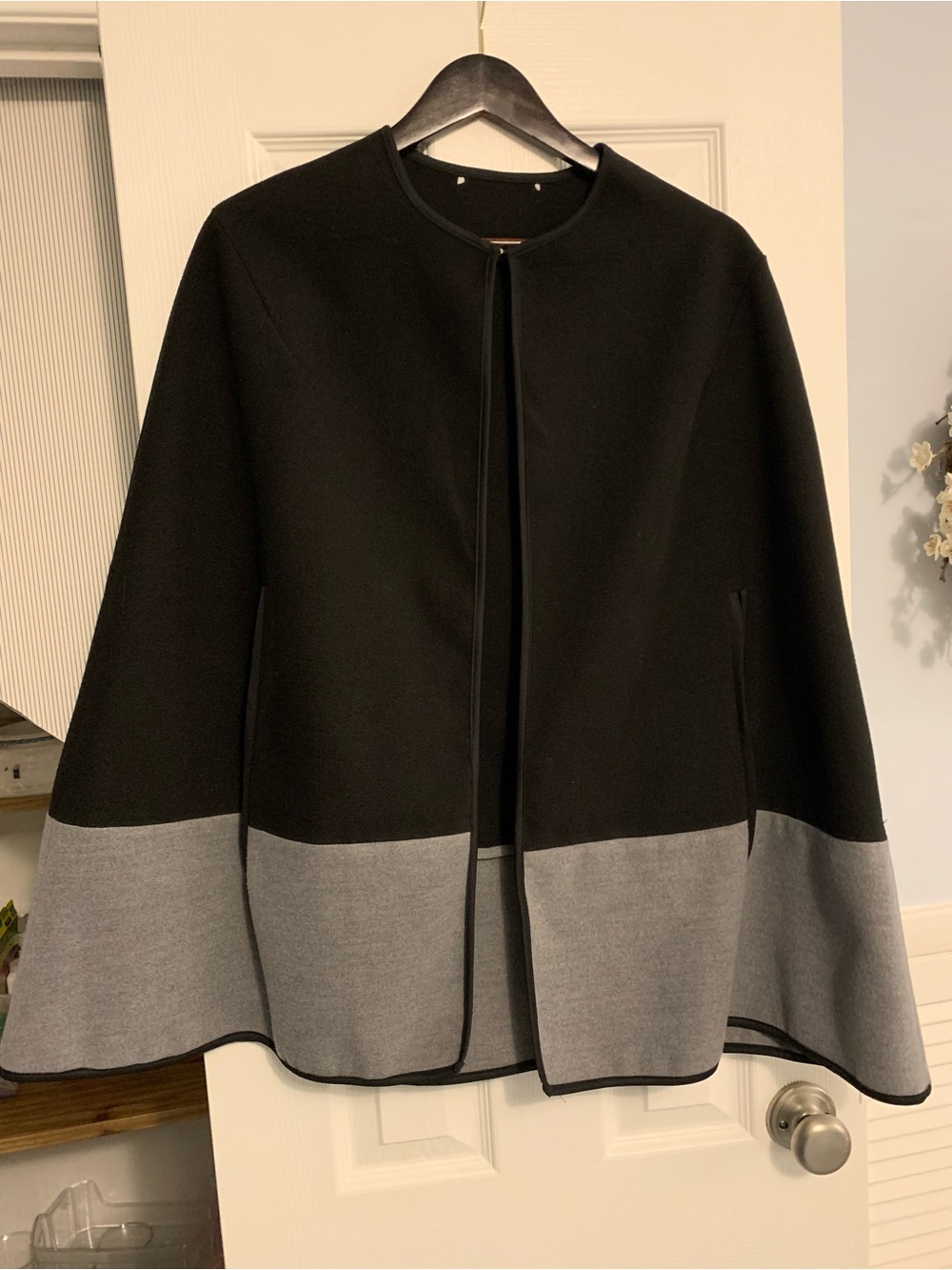 Color blocked black and grey cape. Open-front with piped trim. Two arm openings.